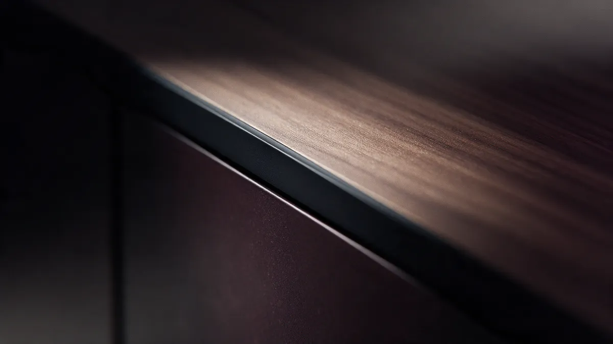 Macro of a walnut veneer top meeting a dark lacquered front along a 2mm edge